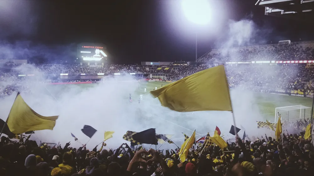 Hinchas con banderas amarillas y humo en un estadio de noche